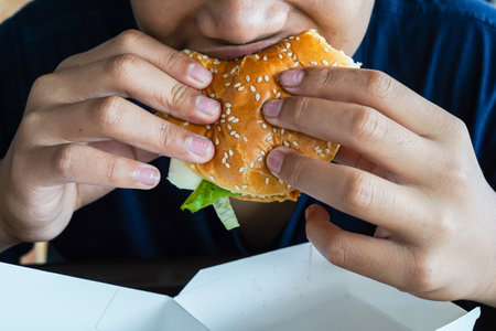 burger in a boy's hand, a hungry boy holds a cheeseburger before eating it, copy spaceの写真素材