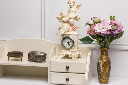 14  December, 2014. Stage studio, Kiev, Ukraine. Modern antique interior of living room. White nightstand with carved  vintage boxes, clock with angels, vase with flowers.のeditorial素材