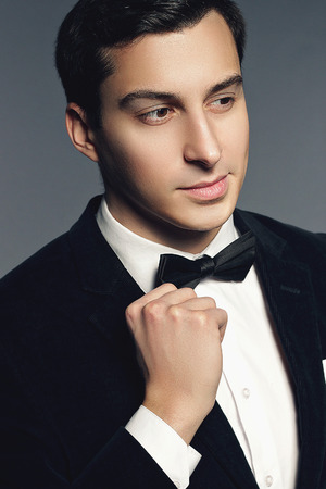 Close-up portrait of handsome elegant young man in black suit, bow tie and shirt on white background. Fashion model studio shooting. Manhood and sexuality. Luxury style.の写真素材