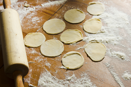 Circles of dough and rolling pin on the wooden table. Homemade process of preparation Russian, Belarussian, Ukrainian meals "vareniki", "pelmeni" (it can be used for dumplings, ravioli, tortellini as well).の写真素材