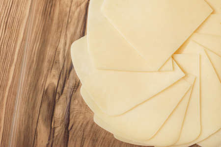 sliced yellow cheese on wooden table and in transparent plate at home, made of delicious milk