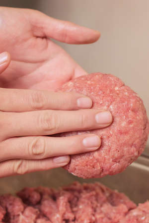 person taking raw minced beef, veal or pork to cook hamburgers fast food on a wooden table in the...