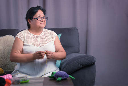 elderly woman 60 year old latin grandmother knitting happy and comfortable inside her homeの写真素材