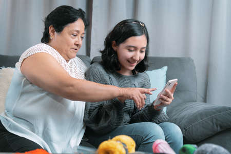older woman 60 year old latin grandmother using cell phone and having fun with her granddaughter...