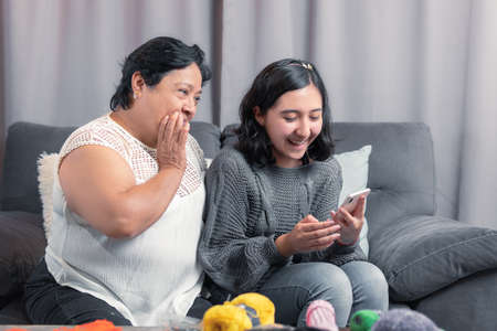 older woman 60 year old latin grandmother using cell phone and having fun with her granddaughter taking photos and watching videosの写真素材