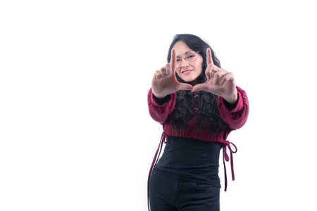 Pretty Latin Hispanic woman with long thick hair wearing glasses on white background indoors doing expressions and gestures, pointing, laughing, happy, focusing, framing and joyful with two hands in frontの写真素材