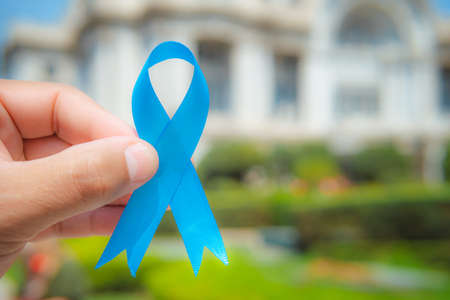 November Prostate Cancer Awareness month, woman holds up a blue ribbon with her hand to support...