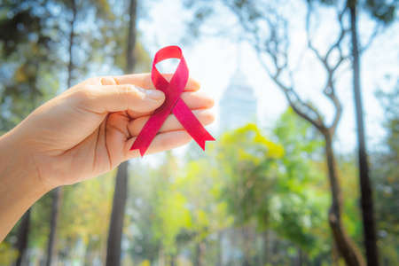 Woman hands hold red ribbon is on the street and background is out of focus. Concept of medicine, World AIDS Day campaign.の写真素材