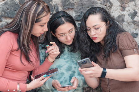 beautiful and young girls having fun and looking at their cell phones, taking photos and walking around the city happy and smiling on a sunny dayの写真素材