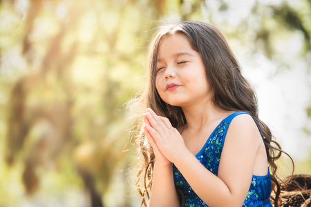 beautiful happy girl playing in the park with blue dress without shoes sitting on tree laughing screaming with happiness in family enjoying children's dayの写真素材