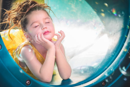 beautiful junior little girl playing in the park in yellow dress laughing with bubbles, screaming with happiness in family enjoying children's dayの写真素材