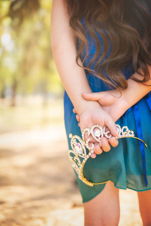 beautiful happy little girl with crown playing in the park in blue dress without shoes laughing screaming with happiness in family enjoying children's dayの写真素材