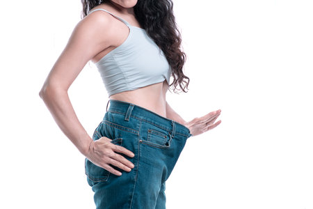 mature beautiful woman measuring her pants and noticing her weight loss happy and motivated stretching out her handの写真素材