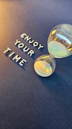 inspiration phrase enjoy your time with hourglass next to it, written in white block lettersの写真素材
