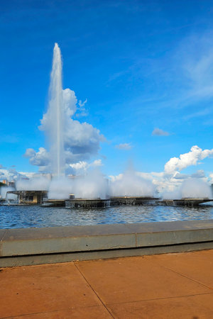 fountain with water jets, in an urban lake in a concrete courtyard and buildings in the backgroundの写真素材