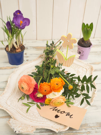 Table with spring flowers and a text message with I love mom on a white wooden background
