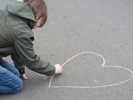 Little boy draws a heart shape with chalk on the groundの写真素材