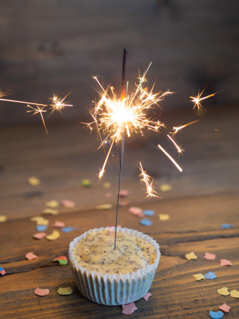 Cupcake with a lighted sparkler on a wooden background with confettiの写真素材