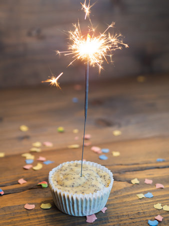 Cupcake with a lighted sparkler on a wooden background with confettiの写真素材