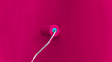 Painting a wall with paint roller. Viva magenta color background. Trend color of the year viva magenta. Selective focus included.の写真素材