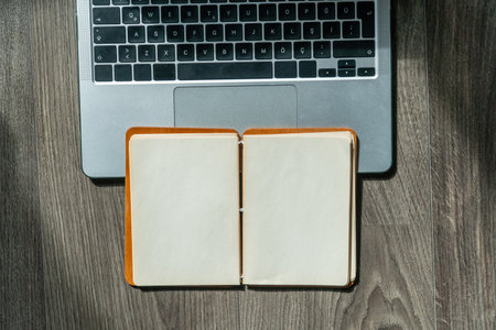 office desk. Laptop and notepad with blank page on wooden table high angle view. Office or study concept with computer and notepad. Copy space for text. Selective focus includedの写真素材