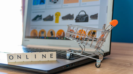 Online shopping concept. Shopping cart or trolley and laptop on wooden table.の写真素材