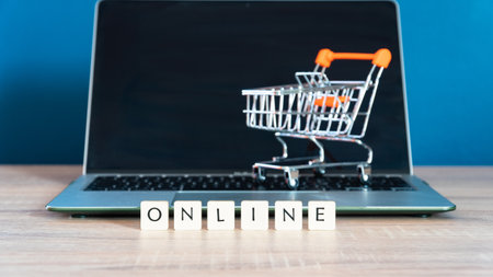 Online shopping concept. Shopping cart or trolley and laptop on wooden table.