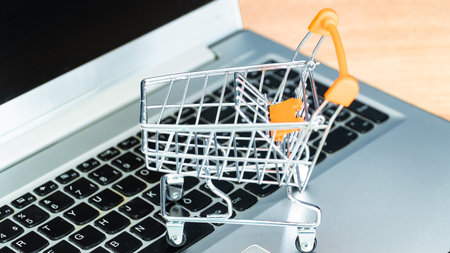 Online shopping concept. Shopping cart or trolley and laptop on wooden table.