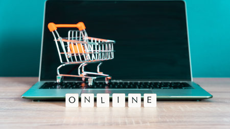 Online shopping concept. Shopping cart or trolley and laptop on wooden table.の写真素材