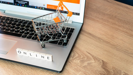 Online shopping concept. Shopping cart or trolley and laptop on wooden table.の写真素材