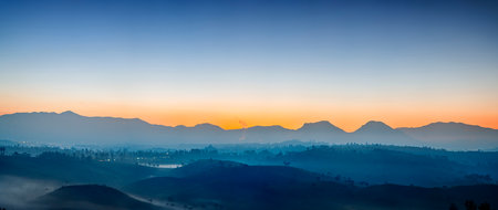 Bathed in soft hues of orange and blue, this breathtaking sunrise over the hills of Cukul in Pangalengan captures the quiet majesty of nature awakening. Gentle silhouettes of the mountains stand in contrast to the glowing sky, while wisps of mist or smoke rise gently from the valley below, adding a touch of mystery. The early light and peaceful atmosphere make this moment a perfect reflection of natureâs calm before the day begins.の写真素材