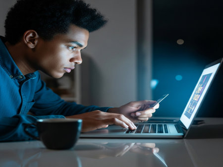 Side view of young African-American man using laptop and tablet at nightの素材