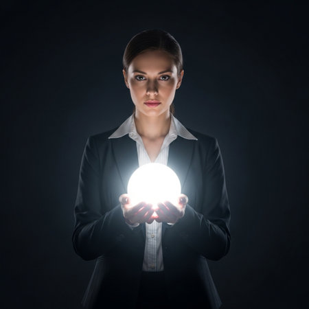 Young businesswoman holding a crystal ball in her hands on dark backgroundの素材