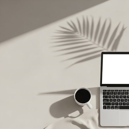 Laptop with blank screen, coffee cup and palm leaf shadow on white wall. Flat lay, top viewの素材