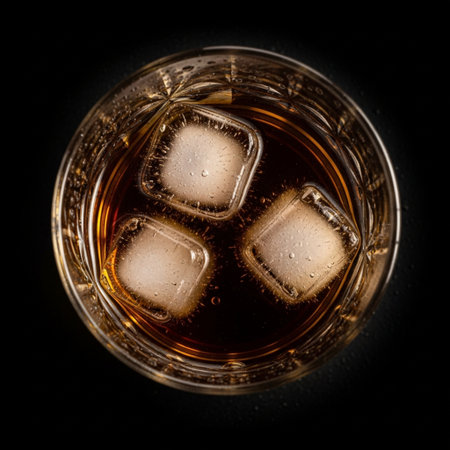 Glass of whiskey with ice cubes on black background. Top view.の素材