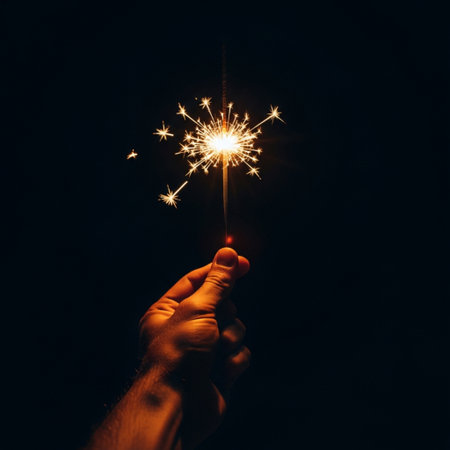 Low angle shot of a hand holding a glowing sparkler against a high-contrast dark night sky.の素材