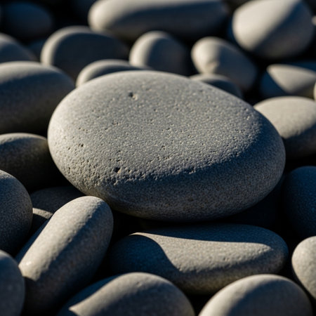 Smooth, gray, worn skipping stones shot in harsh cinematic sunlight with rim lighting and deep shadoの素材