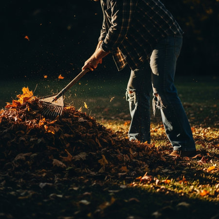Side profile silhouette of a person raking a huge pile of colorful autumn leaves in harsh sunlight.の素材