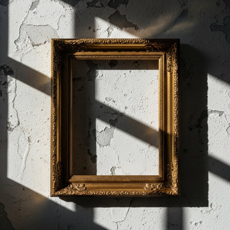 Vintage golden frame on white concrete wall with shadows and sunlight.の素材
