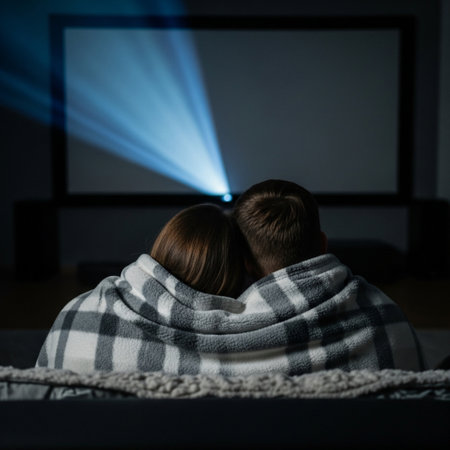 A traditional couple snuggles under a large blanket, watching a movie projected onto a vast home scrの素材