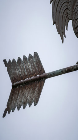 Extreme macro shot of an antique, oxidized metallic weather vane rotating slowly against a stark, paの素材