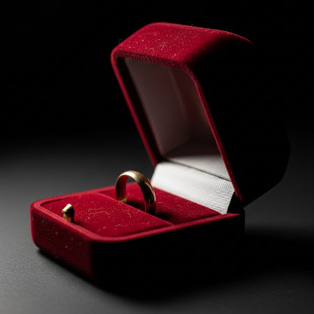 A small, open, dark velvet jewelry box holding a plain gold band ring, captured in a dramatic cinemaの素材