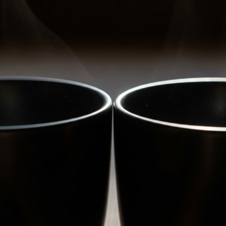 Two matching matte black ceramic mugs, tight close-up on the rims where they connect. The square comの素材