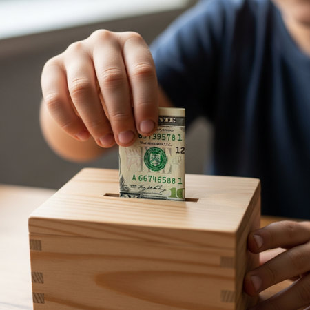 Hero detail shot of a child placing a newly earned dollar bill into a wooden savings box, emphasizinの素材
