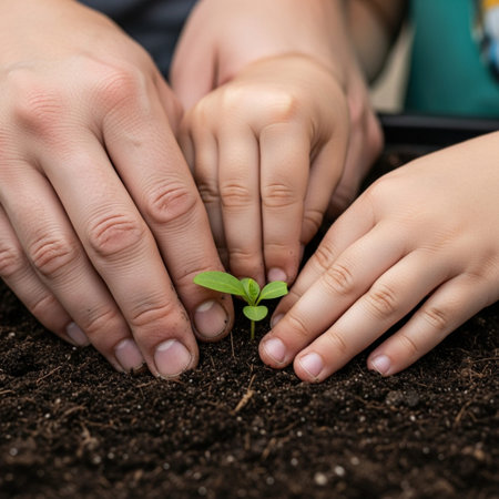 Close-up of adult and child hands planting a green seedling in dark soil. Generational gardening, spring starting, hope, and new life.の素材