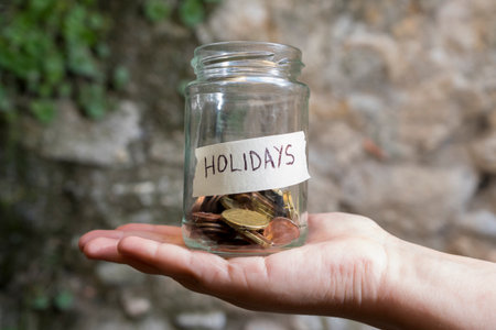 A hand with a glass jar with coins inside it labeledの写真素材