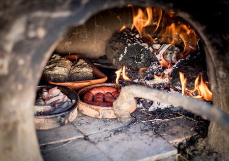 Clay oven with fire and wood to cook chorizo, bacon and leg of lamb.