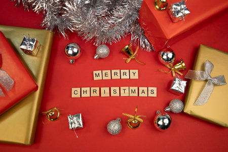Still life with decoration for Christmas, contains decorative gifts, silver Christmas balls, golden bells and gifts wrapped with gold and red paper on a red background.の写真素材