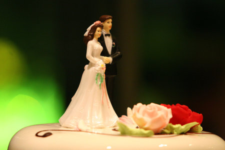 side view close up of small bride and groom figures, a decoration for a wedding cake and two marzipan flowersの写真素材