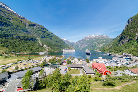 GEIRANGER, NORWAY - 2016 JUNE 14. Beautiful Norwegian fjord with snow on the mountains peaks and green nature with cruise vessels on the fjordのeditorial素材
